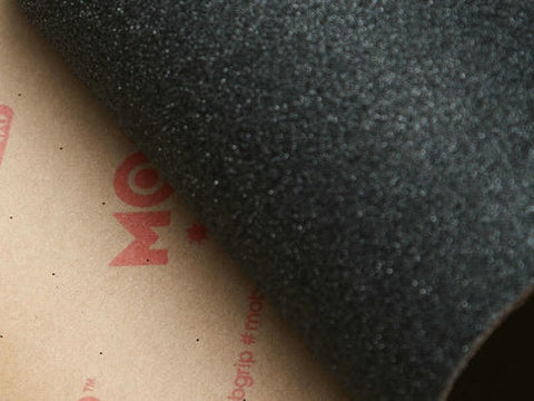Close-up of black skateboard grip tape peeled back to show its printed MOB backing paper